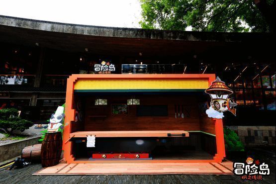 杭州河坊街鼓楼小广场被布置成《冒险岛》主题风格，橙黄配色摊位与立牌引人驻足