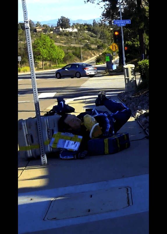 演员背着大量包裹穿越人行道，路人投来好奇目光