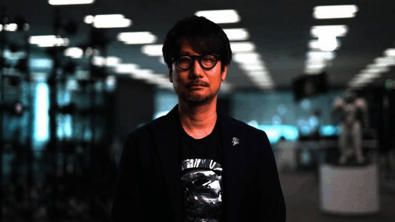 小岛秀夫在访谈现场认真倾听，背景是电影和游戏相关的海报墙