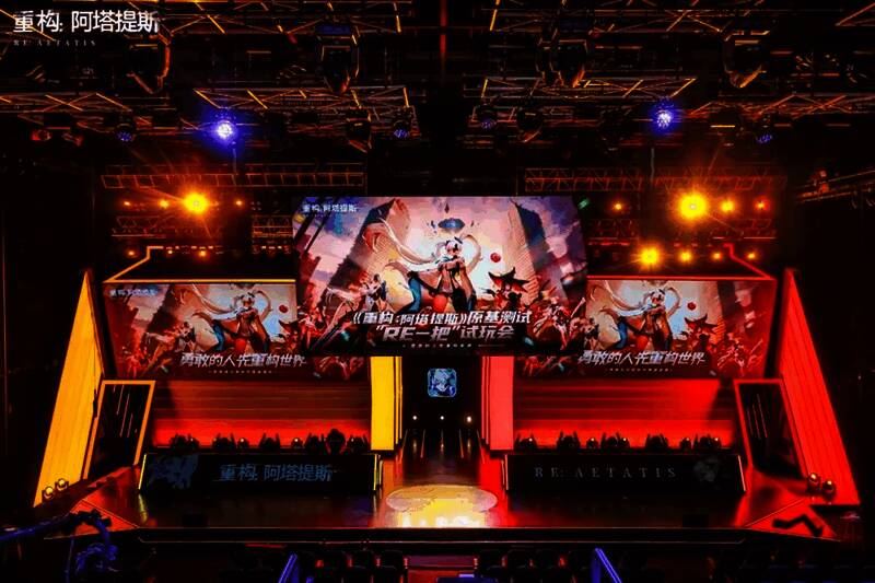 活动现场玩家试玩游戏，气氛热烈，舞台中央有主持人与嘉宾互动