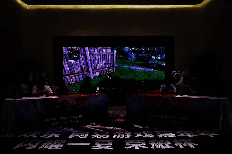 《永劫无间》PK赛现场，选手专注操作手机，大屏实时直播战斗画面，观众围观喝彩