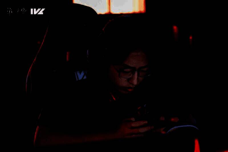 FPX.ZQ_Sxy专注比赛中的特写镜头，眼神坚定，耳机佩戴整齐，背景为IVL赛事舞台灯光