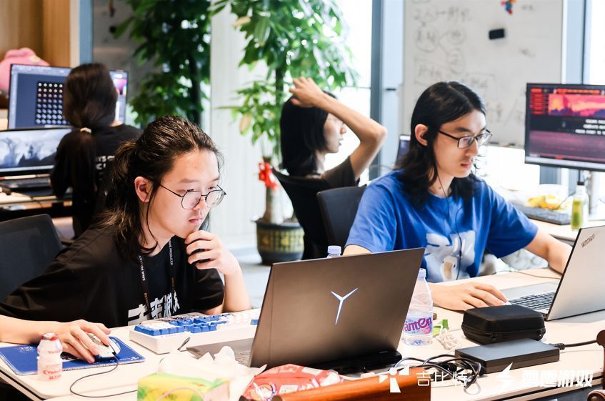 参赛学生在电脑前紧张调试游戏代码，桌上摆放着开发资料与饮料