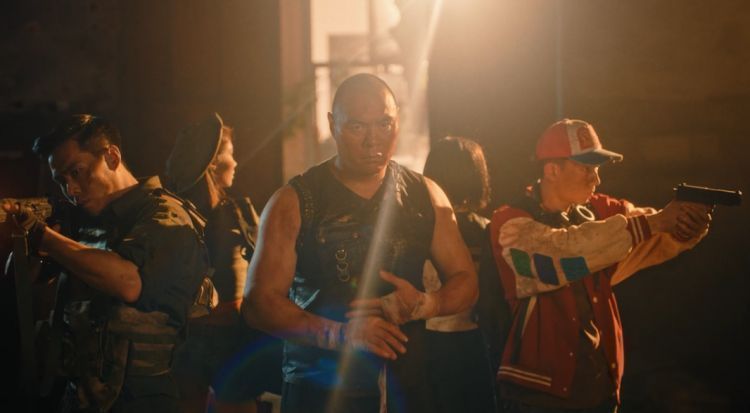 TVC截图：张志磊在废墟中警戒，手持武器，身后是燃烧的建筑与灰暗天空