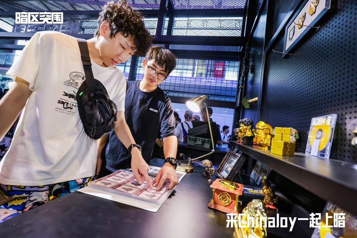 玩家正在参与抽卡互动，展台工作人员递出卡片，背景为游戏风格的灯箱装饰