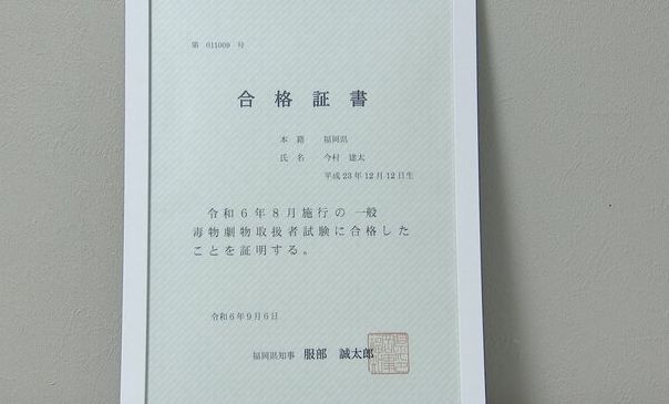 今村建太手持滴管进行精确加液操作，神情专注，背景为通风橱和安全标识