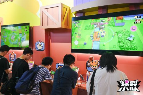 现场玩家专注试玩《爆裂小队》，屏幕上显示5V5对战画面，周围观众围观加油