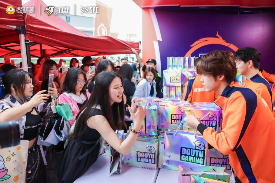 观众在互动区体验游戏试玩，背景为大型赛事宣传海报