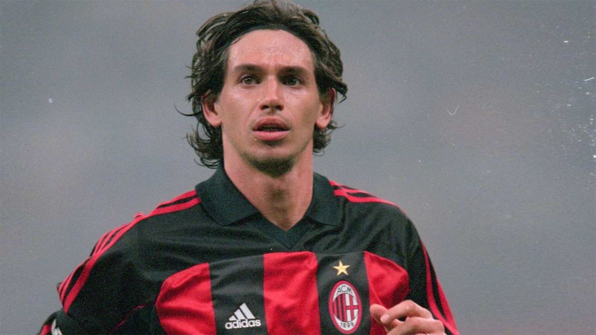 阿尔贝蒂尼身穿AC米兰红黑球衣，站在球场中央，目光坚定，背景为圣西罗球场的璀璨灯光