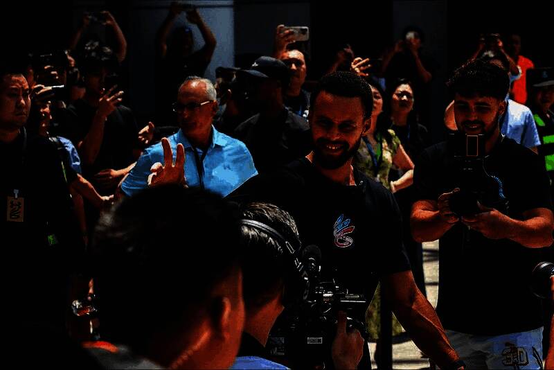 库里在展台前与工作人员交流，神情专注，背景是品牌联合宣传海报