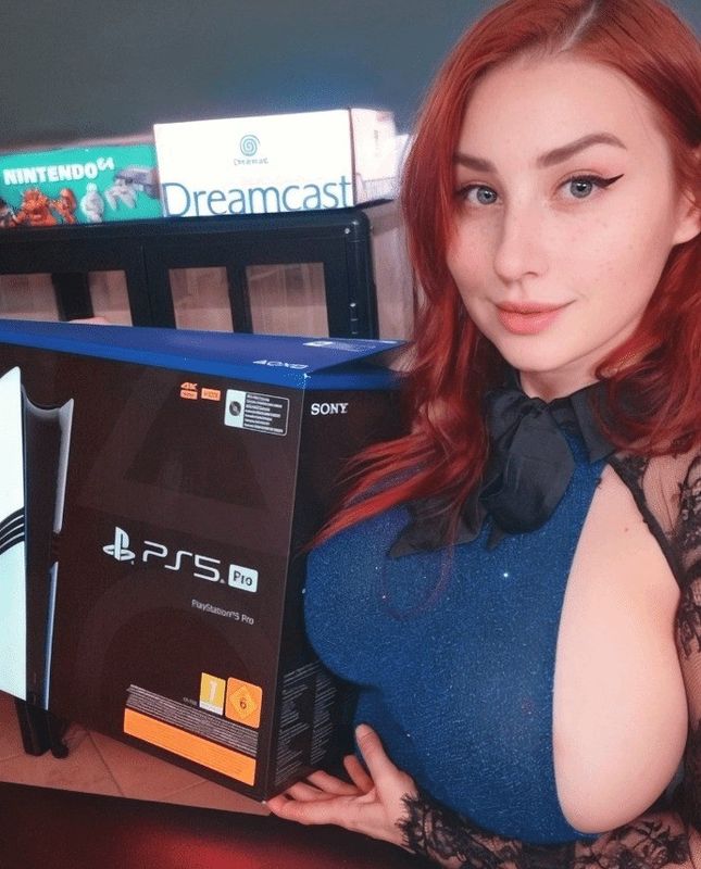 网红推主PureRuby87展示PS5 Pro主机，侧身倚靠桌边，背景中主机清晰可见，氛围俏皮吸睛