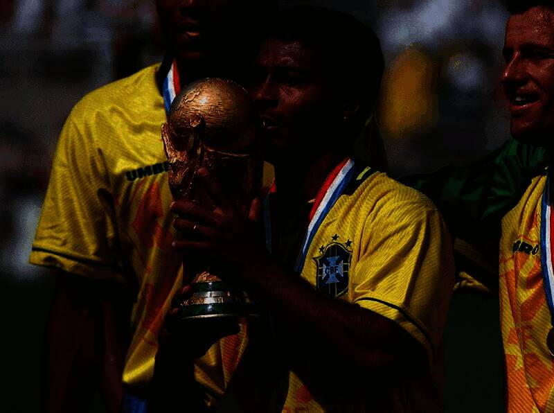 罗马里奥高举世界杯奖杯，笑容灿烂，身旁是欢呼的队友