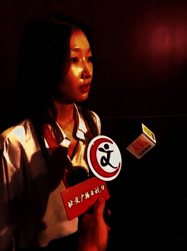 周冬雨出席北京文化论坛现场照片，身穿黑色套装，面带微笑接受采访