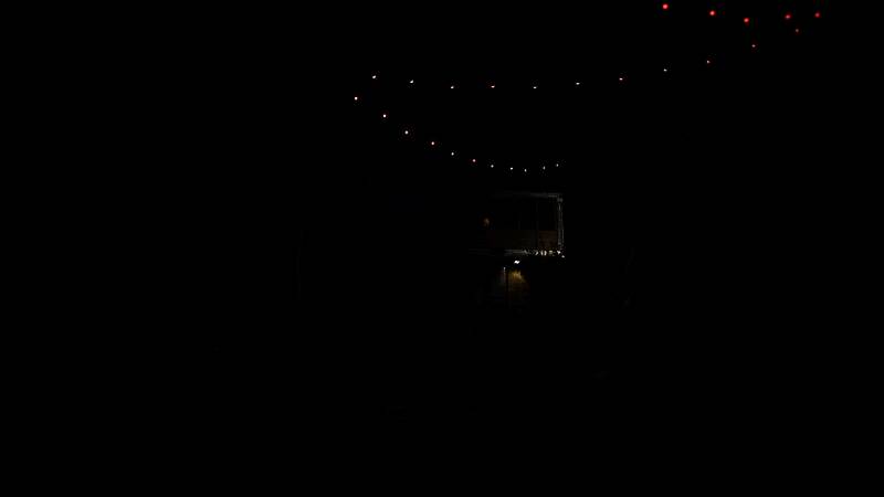 昏暗地下室，铁链悬挂着不明物体，角落堆放人类遗物，暗示曾发生可怕事件