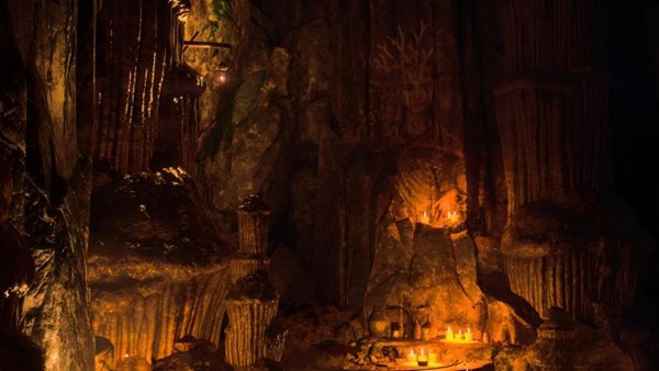 昏暗洞窟内部，角色手持火把照亮前方狭窄通道，墙壁隐约可见古老刻痕