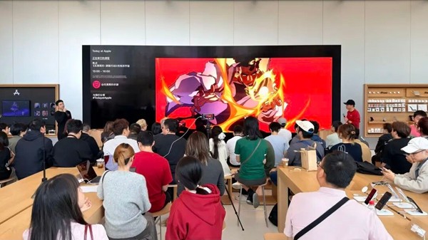 两位主创人员在苹果店内进行演讲，台下观众专注聆听，现场布置融合科技感与游戏元素