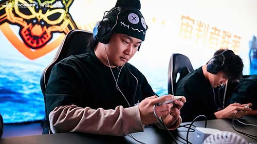 两名选手在比赛现场专注操作设备，面前是双屏实时战况显示