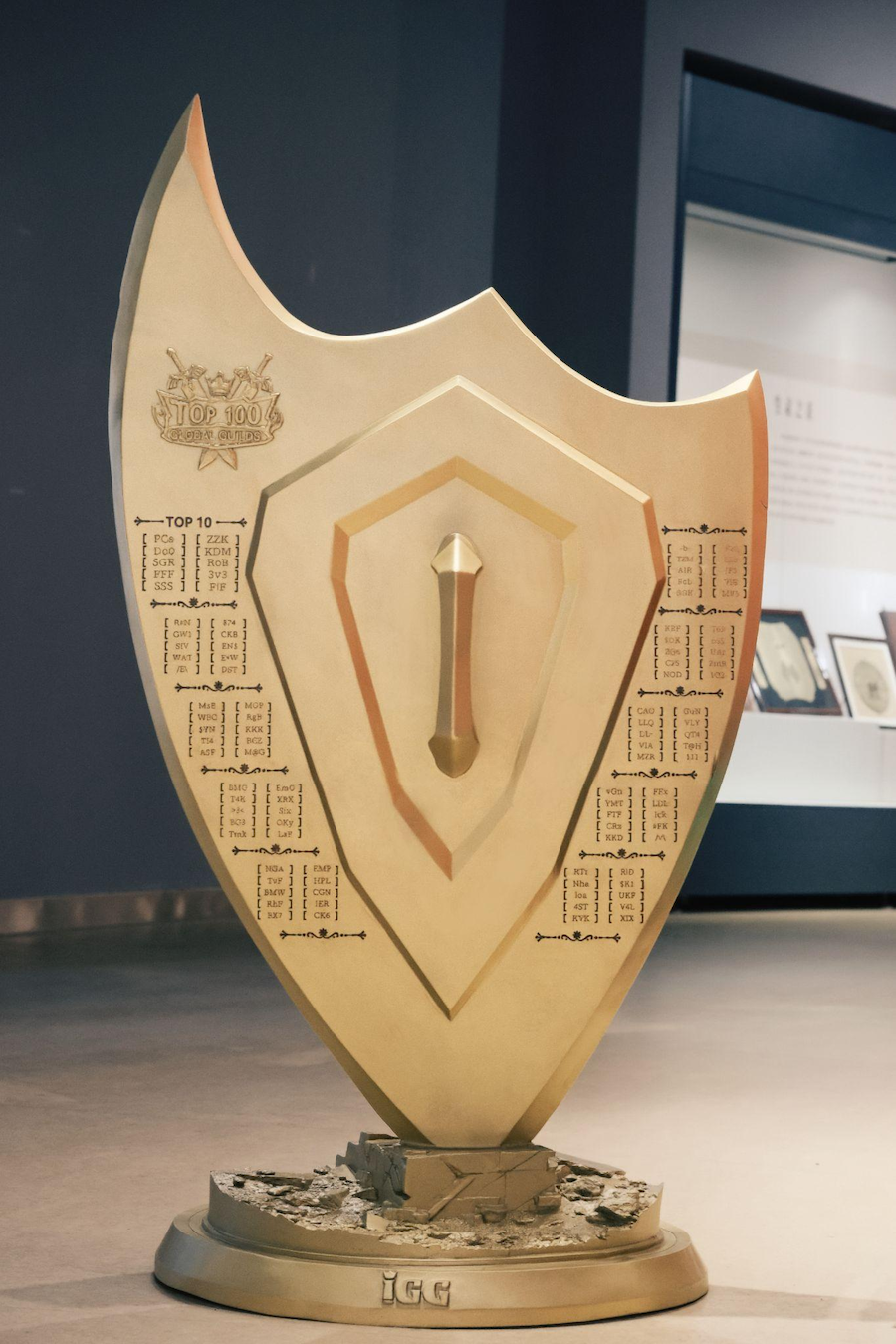 博物馆展出现场：盾牌置于恒温防震展柜中，背景墙展示制作过程纪录片分镜与玩家投稿手稿